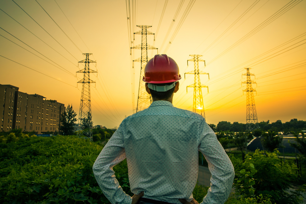 MYRE Energy employee with hard hat and safety glasses smiles for the camera with snowcapped mountains in the distance